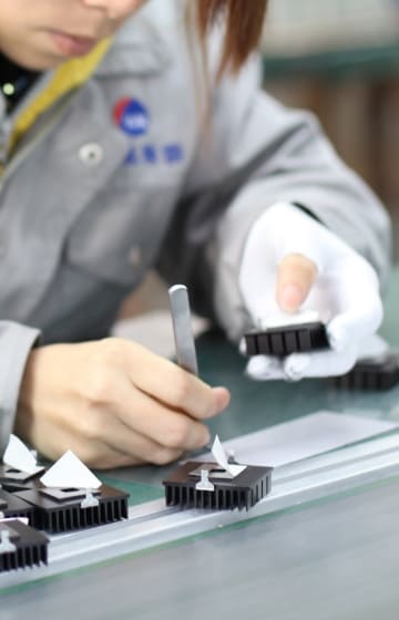 作業服を着た女性が電子部品とピンセットを持って作業している様子