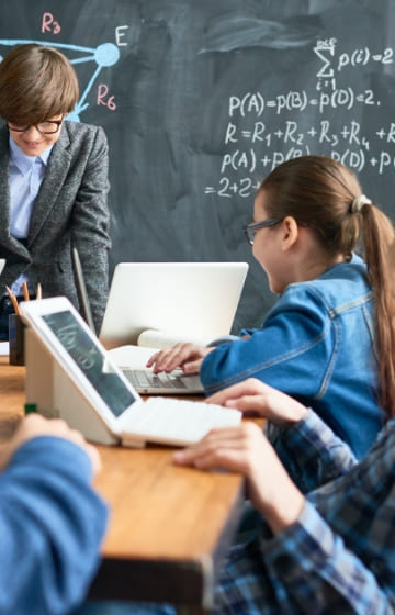 メガネを掛けた先生がパソコンを使って子ども達に授業している様子