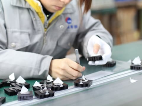 作業服を着た女性が電子部品とピンセットを持って作業している様子